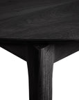 A close-up view of the Bok Round Extendable Dining Table - Black by Ethnicraft, showing its smooth, angled edge and sturdy leg in solid oak against a white background.