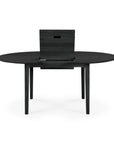 The Ethnicraft Bok Round Extendable Dining Table in black features a modern wooden design with four legs and a raised center that conceals a hidden extension leaf, set against a plain white background.
