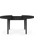 The Ethnicraft Bok Round Extendable Dining Table in black features four legs and is shown partially extended, with a center gap for adding a leaf extension.