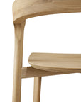 Close-up of the Ethnicraft Bok Counter Stool, showcasing its curved backrest, smooth seat, and angled legs in light-colored wood, set against a white background.
