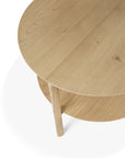 A close-up of the Ethnicraft Bok Coffee Table - Oak shows its round, solid oak design with a lower shelf, three legs, and natural wood grain, photographed against a white background.