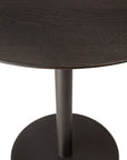 A close-up of the Ethnicraft Blend Dining Table - Brown Oak showcases its dark round tabletop with interchangeable tops and a central metal pedestal base, set against a white background.