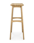 The Ethnicraft Osso Barstool - Oak features three legs, a curved square seat, and two horizontal supports in solid oak with refined European style, shown on a white background.