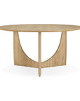 The Geometric Dining Table - Oak by Ethnicraft is a round, solid oak table with a smooth top and a uniquely designed base combining curved and straight lines in a light wood finish.