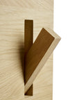 A close-up of Ethnicraft’s Utilitile Wall Hanger, a minimalist solid oak coat hook with a thick, angled plank extending from a light wooden base featuring a rectangular slot, set against a plain white background.