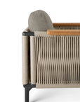 Side view of Ethnicrafts Corbey Outdoor Lounge Chair, showcasing woven rope, black metal legs, light beige cushions, and wooden armrests—a stylish mix of texture and natural materials for any outdoor space.