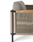 A close-up of the Corbey Outdoor Lounge Chair by Ethnicraft showcases beige woven rope sides, a light wood armrest, gray cushion, and sleek black metal legs—ideal for elevating your outdoor space.