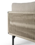 Close-up of the Ethnicraft Corbey Outdoor Lounge Chair features a beige woven rope side panel, soft fabric cushion, and black metal legs—ideal for elevating your outdoor space against a white background.