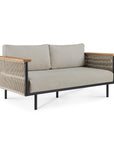 The Corbey Outdoor Lounge Chair by Ethnicraft features light beige cushions, a black metal frame, wooden armrests, and rope side detailing. Its minimalist design brings modern style and comfort to any outdoor haven.