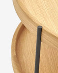 Close-up of two stacked Humla Round Side Tables by Wooden Stories, featuring raised edges and Danish-inspired design, with round wooden tops supported by a vertical black metal rod, shown against a plain white background.