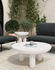 Create a stylish outdoor seating area with two Salma Outdoor Lounge Chairs by Moes in dark gray, quick-dry foam cushions, a round white coffee table, side table, potted plants, and a light patterned rug on a patio with cream walls and arched glass doors.