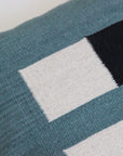 A close-up of Ania Brzeski’s Pillow 04: Blue + Black, handwoven from locally sourced wool. It features a modern geometric pattern in blue, black, and off-white with visible texture highlighting its striking design.
