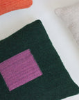 Three handwoven pillows are shown: orange, beige, and Pillow 02: Green + Purple by Ania Brzeski, featuring a dark green base with a large purple square design—all crafted from locally sourced wool.