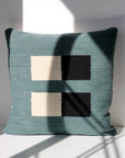 Pillow 04: Blue + Black by Ania Brzeski is a handwoven decorative pillow with a teal background and vertically stacked cream and black squares, highlighting a modernist design.