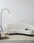 A modern living room with a curved white sofa, round coffee table, floor lamp, and neutral decor. White walls and the Armadillo&Co Acacia Rug in Fawn over a beige floor create a clean, contemporary look.