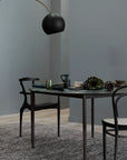 A modern dining area with a dark rectangular table for two, black chairs, minimalist decor, and a large black overhead lamp stands against gray walls and features the Armadillo&Co Acacia Rug - Sable.