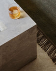 A glass of amber whisky with a large ice sphere rests on a light gray stone table beside the Armadillo&Co Willow Rug - Cypress, its jute and wool fibers blending green and beige hues.