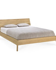 The Ethnicraft Air Bed, crafted from light European oak, features a slanted headboard and comes styled with a beige and white comforter plus two matching pillows.
