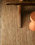 The Armadillo&Co Mojave Rug - Natural sits beneath a rustic wooden table with a bowl and beside a round peach stool, adding warmth and coziness to the space.