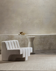 Minimalist room featuring a sculptural white chair, the Armadillo&Co Sherpa Rug in Sand, a round pedestal table, and a shallow bowl with dried branches against a neutral plaster wall.