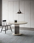 Minimalist dining area featuring a round marble table, black wooden chair, glass of water, and small black container on the table, all atop the Armadillo&Co Corsica Rug - Capri, set against a plain wall.