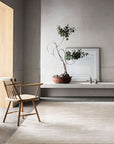 Minimalist room with neutral tones featuring a wooden chair, a large potted plant on a white bench, framed abstract art, and small decor on the Eden Rug - Nougat by Armadillo&Co, crafted from hand-knotted wool.