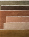 A neatly stacked display of Armadillo&Co Eden Rug - Verona in earth tones like brown, beige, and olive, each hand-dyed in wool and accented with a light stitched border.