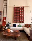 A cozy living room features a white sectional sofa, colorful pillows, and the Bolinas Coffee Table - Claro Walnut by SOBU. A potted plant, geometric wall art, ladder, and textured rug complete the warm, earthy décor.