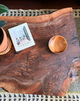 The Bolinas Coffee Table - Claro Walnut by SOBU, handmade in Oakland, is styled with a potted plant, Live Beautiful book, and a wooden bowl atop a patterned rug—ideal for modern design lovers.