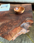 A close-up of the SOBU Bolinas Coffee Table - Claro Walnut, handmade in Oakland with a natural, live edge; a wooden bowl and books rest on top, showcasing its modern design and rich walnut grain.