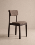 The Noki Dining Chair | Fabric by Wooden Stories features a modern solid wood frame with a curved backrest and fully upholstered seat and back, shown here against a neutral beige background. Its contract-grade construction ensures lasting durability for both residential and commercial environments.