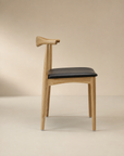 The SOBU Copenhagen Dining Chair in White Ash features a minimalist solid wood frame, black cushioned seat, and a curved backrest, shown in profile against a neutral beige background.