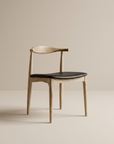 The Copenhagen Dining Chair by SOBU features a minimalist mid-century design with a curved backrest, black leather seat, and solid white ash wood, shown against a plain beige background.