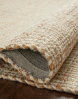 A close-up of the Loloi Cornwall Rug in Ivory/Natural, showcasing its textured pattern and thick wool yarn, partially folded on a dark wooden floor.