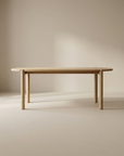 The Wooden Stories Cove Dining Table | Light Oak features solid American oak with rounded edges and four cylindrical legs, shown against a neutral beige background in a softly lit room.