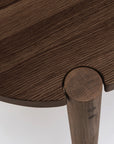 Close-up of the Cove Dining Table | Espresso Oak by Wooden Stories, featuring a round top, curved leg joint, and showcasing solid American oak grain with precise contract-grade craftsmanship.