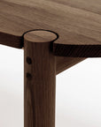 Close-up of Wooden Stories' Cove Dining Table | Espresso Oak shows precise joinery where the solid oak tabletop meets a round leg. The wood grain and craftsmanship highlight its minimalist, modern design.