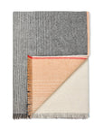 The Carte Postale Throw - Grey by Elvang Denmark showcases Fair Trade craftsmanship with gray and white stripes, solid gray and beige panels, a cream and peach reverse in one corner, and stylish fringed edges.