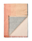 The Carte Postale Throw - Red Grey by Elvang Denmark is a Fair Trade certified, rectangular alpaca blanket with color-blocked peach, gray, cream, and red stripes. Features short multicolored fringe and one folded corner showing the reverse.