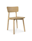 The Casale Dining Chair by Ethnicraft features light European oak, a flat seat, angled legs, and a subtly curved backrest, offering classic refinement against a white background.