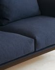 Close-up of the Cherry Sofa 95" by Wooden Stories, featuring dark blue fabric upholstery, two seat cushions, Danish-inspired lines, and slim dark metal legs—ideal for a modern living space with a light-colored floor.