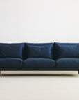 The Cherry Sofa | Fabric by Wooden Stories features plush cushions and clean Danish lines, set against a white wall on a light floor—perfect for adding modern style to any living space.