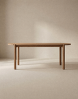 The Wooden Stories Cove Dining Table | Latte Oak features a minimalist design, meticulously crafted from solid American oak with rounded edges and four substantial cylindrical legs. Displayed against a neutral beige background, it is ideal for both residential spaces and contract-grade environments.
