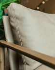 Close-up of the Troubadour Lounge Chair | Leather • Light Oak by Wooden Stories, showing a light beige leather cushion and smooth oak armrest, with a green plant in the background—evoking timeless Danish design.