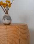 A small rustic vase with yellow billy ball flowers rests on the SOBU Saturn Side Table - Natural, crafted from solid pine with visible grain and natural cracks, against a plain light-colored background.