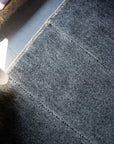 A close-up of the HIMALAYAN HERMITAGE Radhi Rug - Silver shows its textured Nepali wool on a light floor, sunlight highlighting the hand-woven edge near a window while shadows fall across the rest.