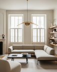 A bright, modern living room with cream walls, a large L-shaped sofa, a SOBU Mars Live Edge Coffee Table in Black Ash, a minimalist pendant light, built-in shelves with decor, and two tall windows with white shutters.