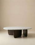 The Eden Coffee Table by Wooden Stories features a smooth oval Carrara marble top and three dark, rounded solid American oak supports, set against a neutral beige background.