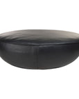 The Fable Ottoman | Leather by Wooden Stories is a large, round black leather ottoman with a smooth surface and subtle side stitching, presented against a white background—showcasing refined Danish furniture design.