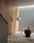 A modern minimalist interior with a wooden accent wall, sculptural floor lamp, round textured stool, and a vase with a single branch, all set on the Armadillo&Co Faroe Rug in Muscovado.